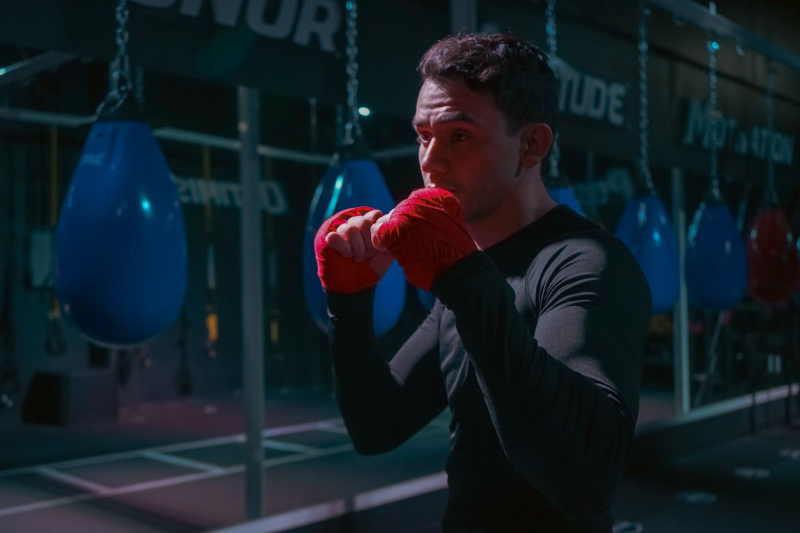Boxer in red gloves working the heavy bag under blue gym light