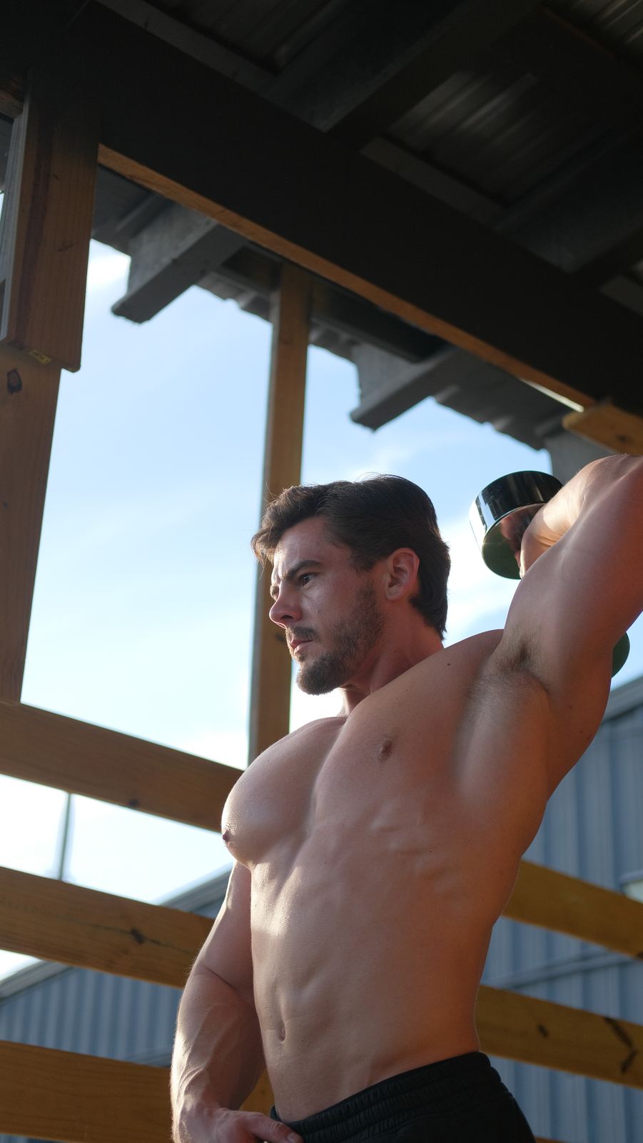 Bodybuilder stretching outdoors under a wooden frame